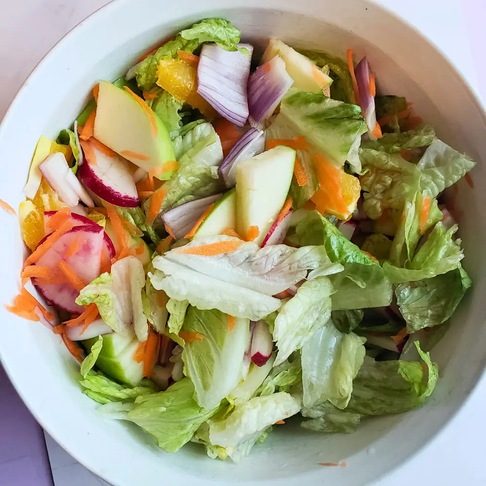 A vibrant Citrus Harvest Salad in a large bowl, featuring mixed greens, sliced apples, fresh orange segments, and grated carrots. The salad is topped with crunchy toasted walnuts and a zesty orange-honey vinaigrette. Professional real food food photography.