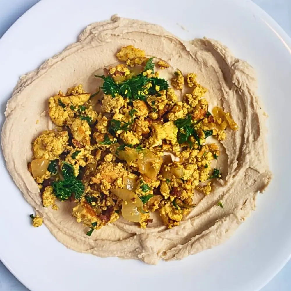 Homemade tofu shawarma served over a creamy bed of hummus on a plate.