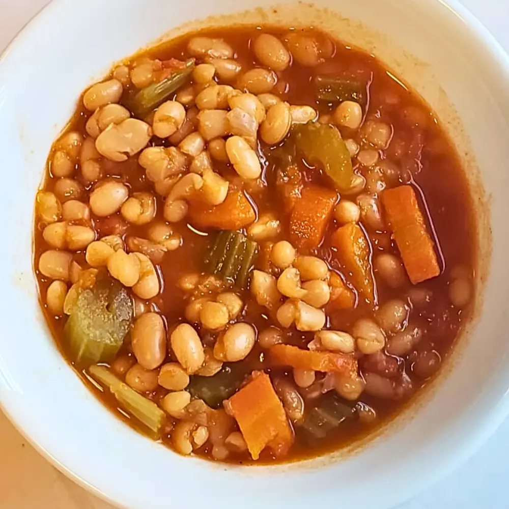Traditional Greek Fasolada white bean soup in a ceramic bowl, garnished with olive oil and fresh herbs.