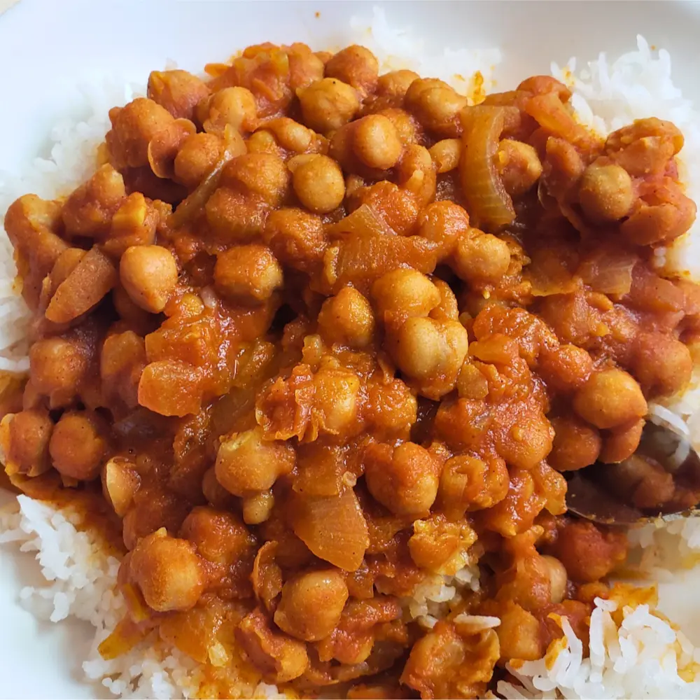 A steaming bowl of rich Mediterranean chickpea tomato stew, served over fluffy white rice.
