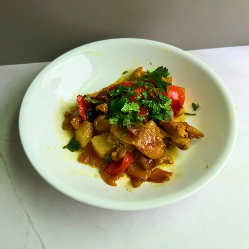 A white bowl filled with Mediterranean pineapple chicken thighs in a glossy date syrup glaze, topped with fresh parsley, by The Promised Cook.