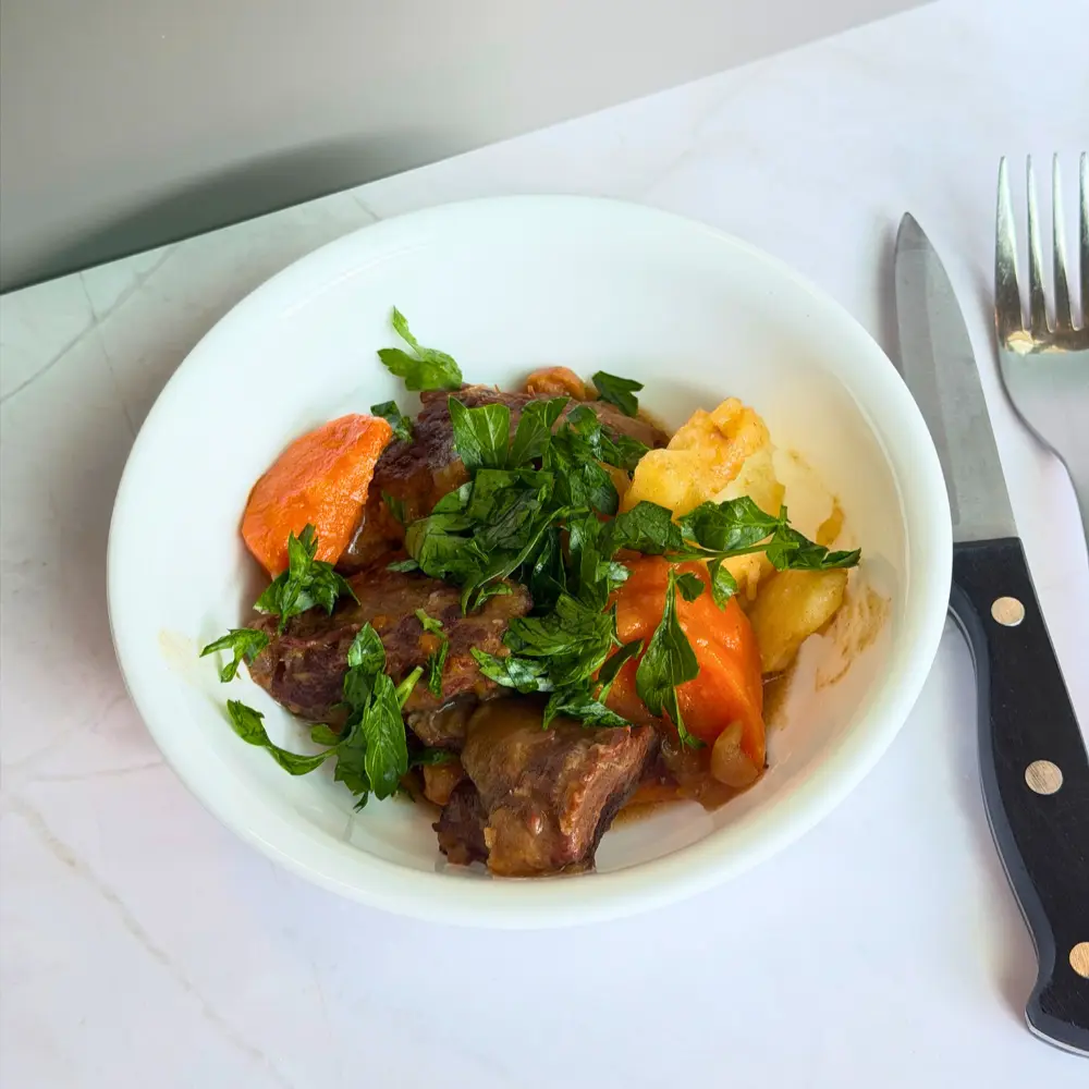 A close-up of tender Instant Pot beef stew with chickpeas and carrots in a rich date syrup sauce, garnished with fresh parsley and a squeeze of lemon by The Promised Cook.